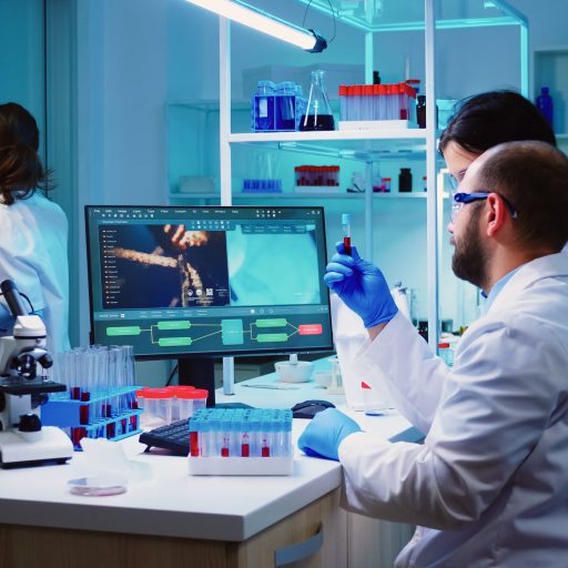 Microbiologist doctor taking a blood sample tube from rack with machines of analysis in the lab background. Doctors examining vaccine evolution using high tech researching diagnosis against covid19