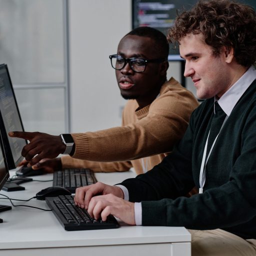 Programmer pointing at computer monitor with codes and talking to his colleague while they working with computer program in team